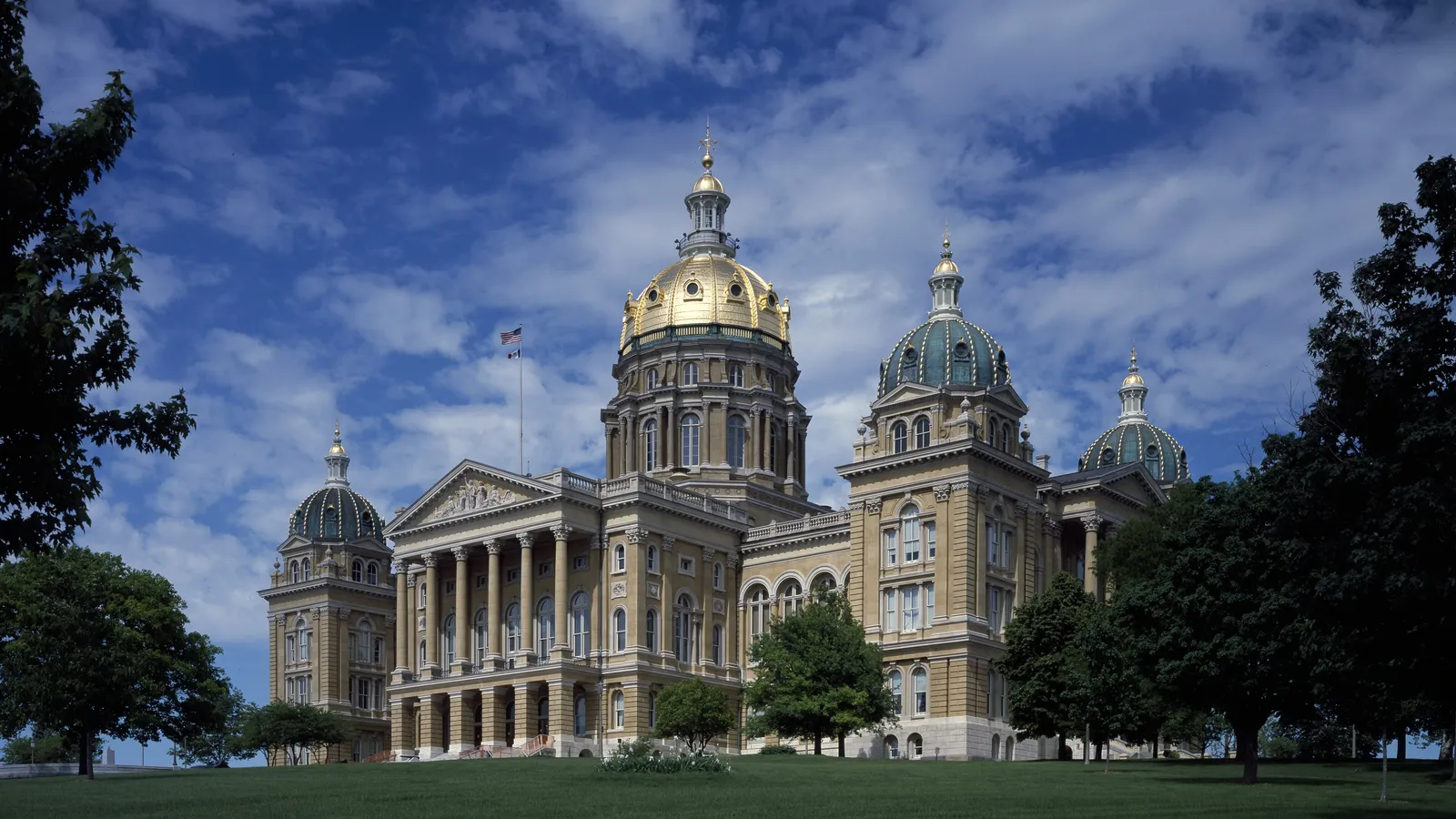 The Iowa State Capitol in Des Moines, with its gold central dome and four smaller domes, seen across a green lawn under a blue sky
